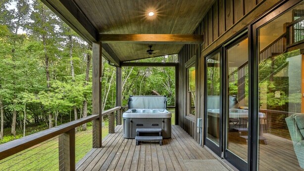 A wooden deck with a hot tub, glass doors, and a forest view. - FightingTown Escape | Blue Ridge, GA (McCaysville)