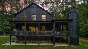 Une maison en bois à deux étages, dotée d’un balcon, de fondations en pierre et d’une cheminée.