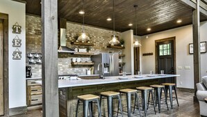 A kitchen with a central island, bar stools, hanging pendant lights, and a brick wall. - FightingTown Escape | Blue Ridge, GA (McCaysville)