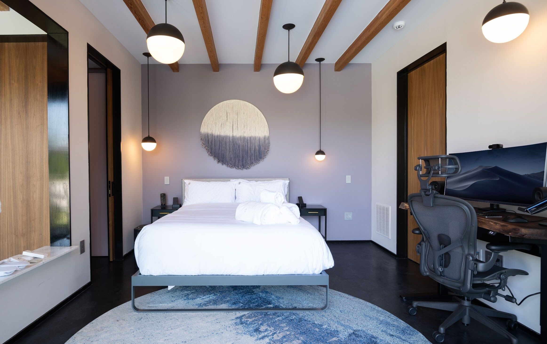 A modern bedroom with a large bed, a desk with a computer, and pendant lights.