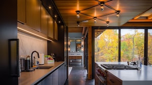 A modern kitchen with a central island, wooden cabinets, and a view of autumn trees through large windows. - Hudson Ridge / Hot Tub, Fire Pit & Fireplace (Hudson)
