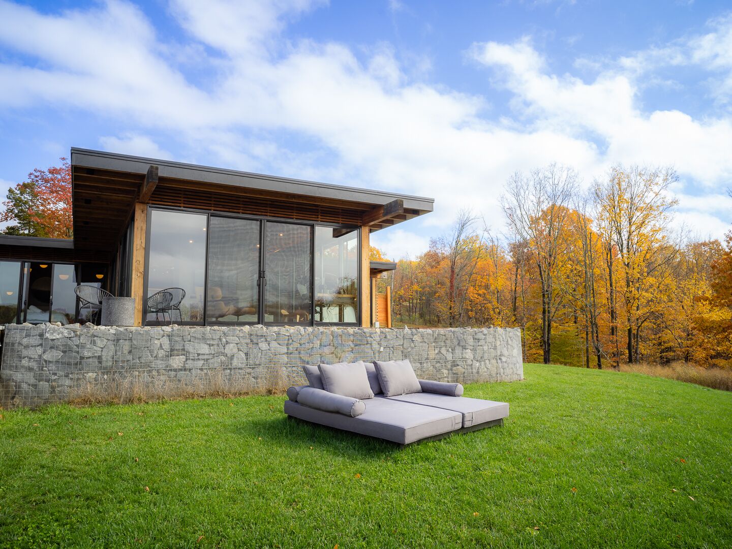 A modern house with a stone wall, a glass door, and a grey outdoor sofa.