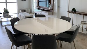 Een moderne eetruimte met een ronde tafel, zes stoelen, een kroonluchter en een groot raam met uitzicht.