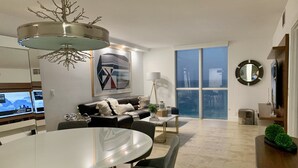 Een moderne woonkamer met een eetgedeelte, grote ramen en een flatscreen televisie.