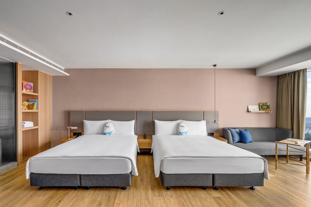 A hotel room with two beds, a sofa, a small table, and a bookshelf.
