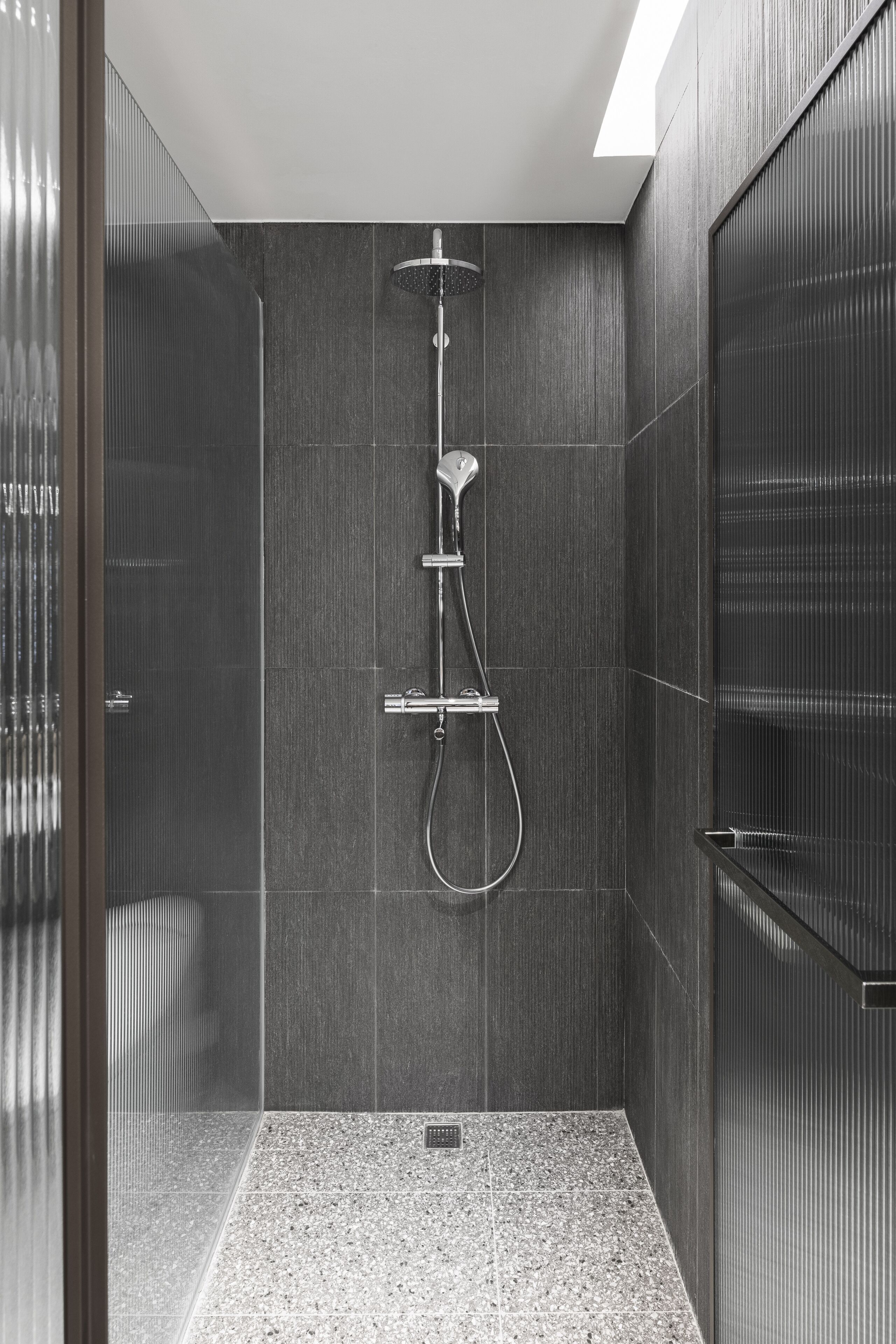 A modern shower with a handheld showerhead and a wall-mounted faucet.