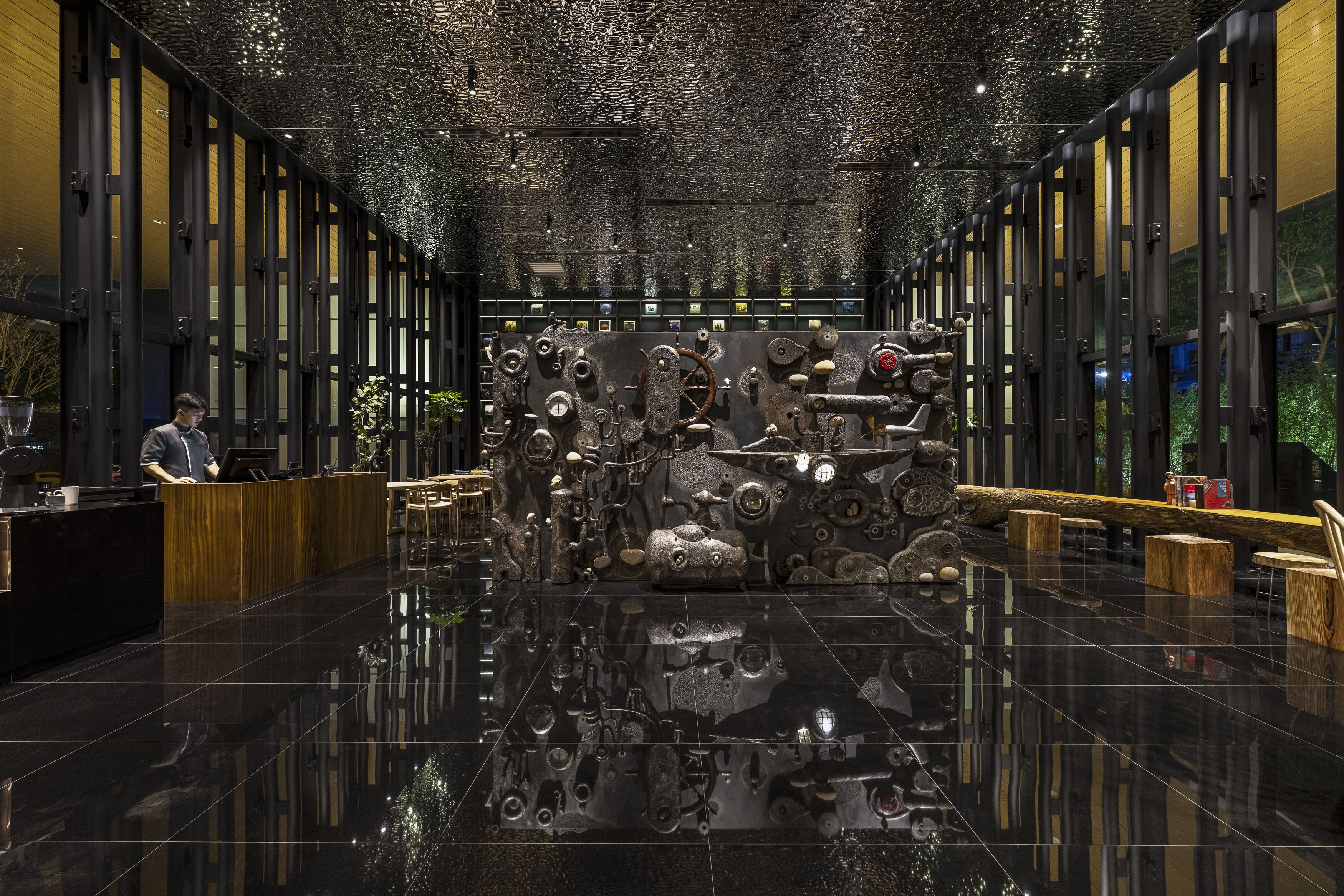 A modern lobby with a reflective black floor, a reception desk, and a unique wall installation of mechanical parts.