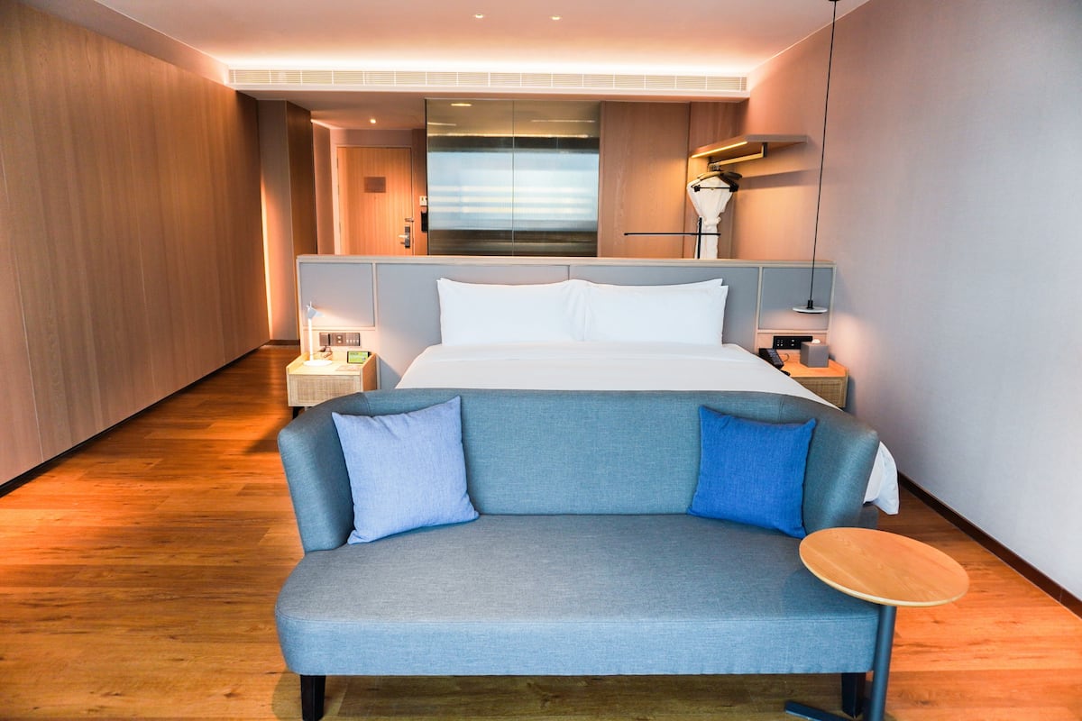 A modern hotel room with a large bed, a sofa, and a bedside table.