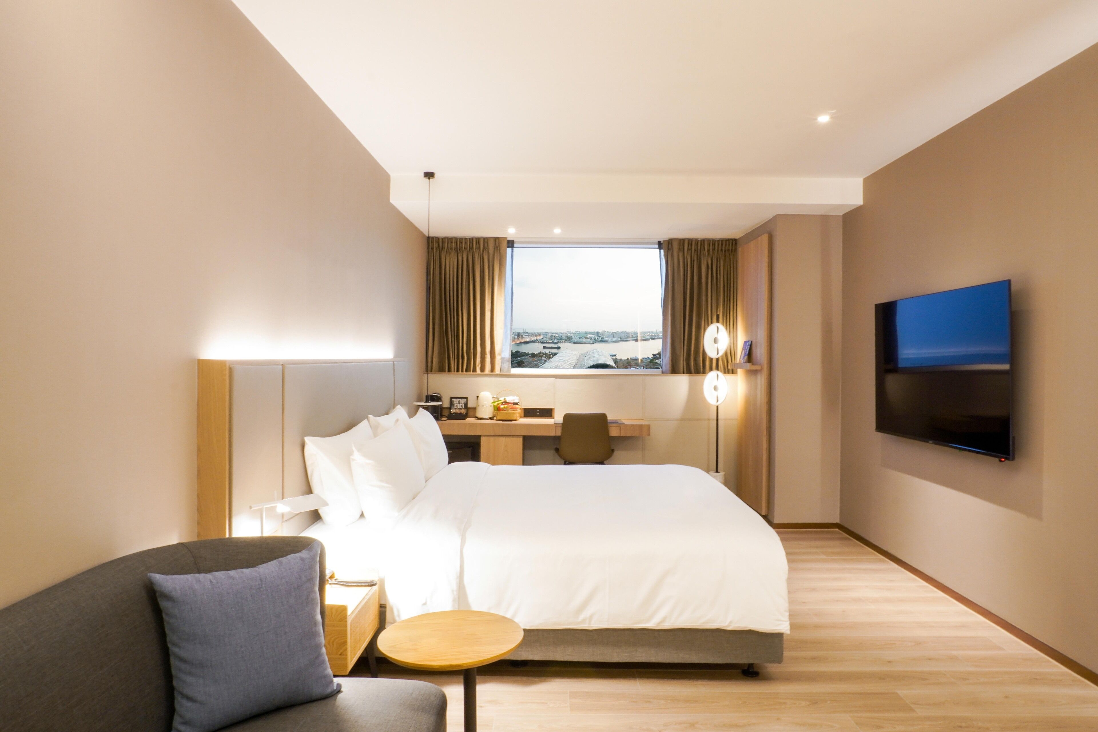 A hotel room with a bed, a desk, a chair, a TV, and a view of the city.