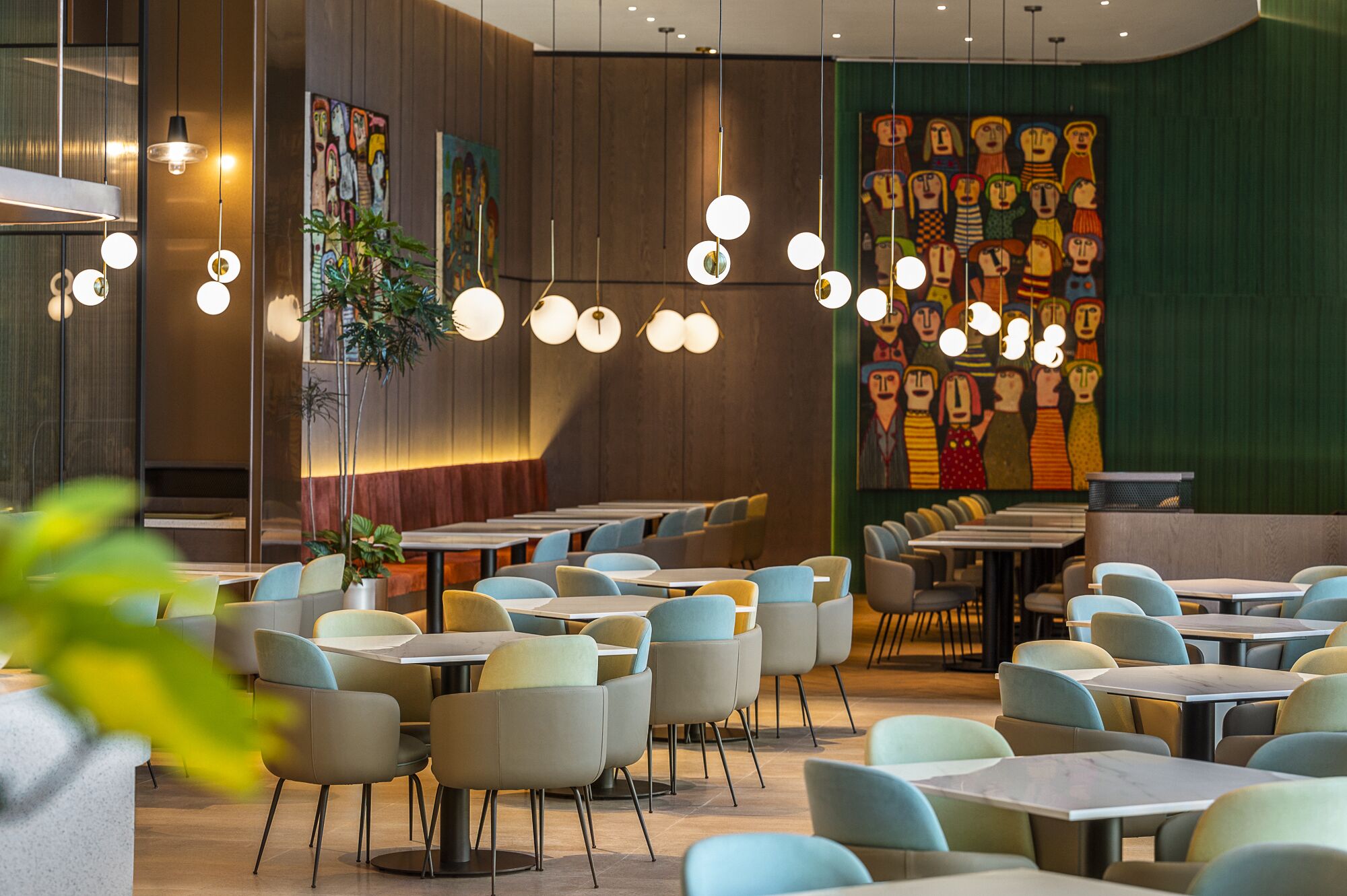 Un interior de restaurante moderno con mesas y sillas redondas, lámparas colgantes y arte abstracto colorido en las paredes.