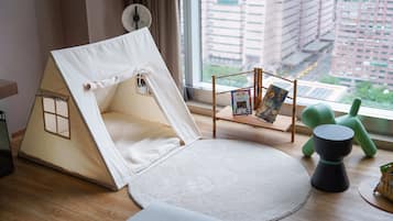 A room with a large window, a white tent-like structure, a round rug, a small table with a book, and a green chair.