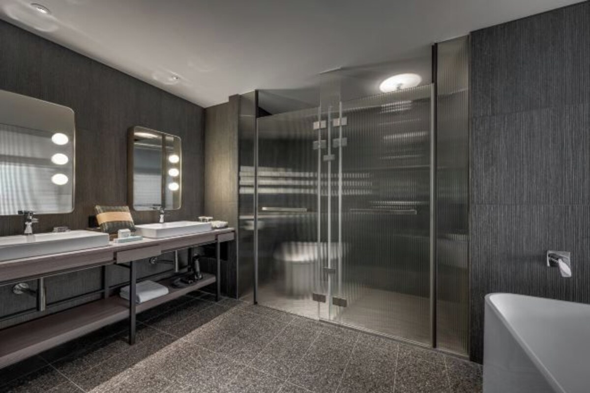 A modern bathroom with a glass shower enclosure, a vanity with a mirror and lights, and a bathtub.