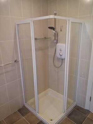 Une cabine de douche fermée par des parois en verre, dotée d’un pommeau de douche à main et d’un panneau de commande fixé au mur.