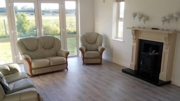 A spacious living room with a fireplace, two sofas, and a large window offering a view of the outdoors. - Entire House, Self Catering in Castlerea Ireland (Castlerea)