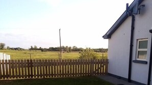 A fenced backyard with a white building, a wooden fence, and a grassy field. - Entire House, Self Catering in Castlerea Ireland (Castlerea)