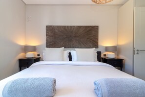 A hotel room with a large bed, two bedside tables with lamps, a wall-mounted artwork, and two towels on the bed.