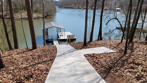A concrete pathway leading to a dock by a lake, surrounded by trees and dry leaves.