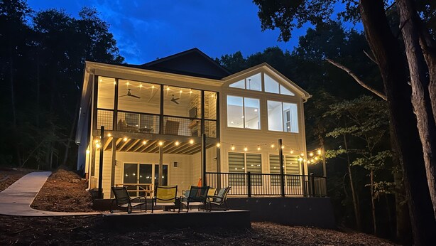 A two-story house with a balcony, string lights, and a deck with chairs.