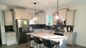 A modern kitchen with white cabinets, a large island with bar stools, stainless steel appliances, and pendant lighting.