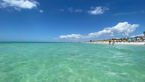 Una playa con aguas turquesas cristalinas, una orilla arenosa y algunas personas a lo lejos.