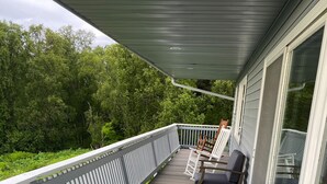 Eine überdachte Terrasse mit Holzboden und weißen Geländern, mit zwei Holzstühlen und Kissen.