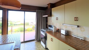 A kitchen with a gas stove, oven, and a toaster. There is a sliding glass door leading to an outdoor area. - 37 Brady Street Mallacoota (Mallacoota)