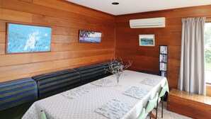 A cozy room with wooden walls, a dining table with a floral tablecloth, a vase with branches, and a bookshelf. - 37 Brady Street Mallacoota (Mallacoota)