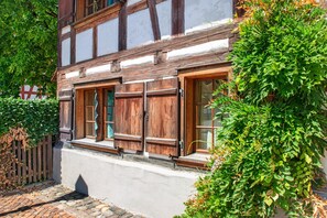 Un bâtiment traditionnel à colombages, doté de volets en bois, d’un chemin pavé et d’une végétation luxuriante.