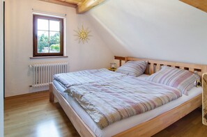 A bedroom with a wooden bed, a window with a view, a radiator, and a sun-shaped wall decoration.