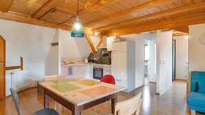 Une pièce spacieuse avec un plafond en bois, une table à manger avec des chaises, un coin cuisine et un canapé bleu.