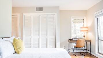 A bedroom with a bed, a desk with a chair, and a window with blinds.