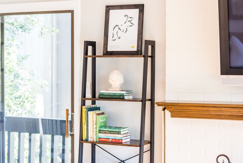 A bookshelf with books and a decorative item, a framed picture above it, and a fireplace in the background.