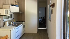 Une petite cuisine équipée d’un four à micro-ondes, d’une cuisinière et d’un évier. On peut voir une chaise en bois sur la gauche.