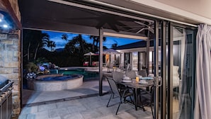 An outdoor patio area with a pool, seating, and a grill. - Elegant 4BR Pool Home + Guest House | Walk to Beach (Naples)