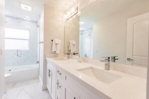 Une salle de bain moderne avec un grand miroir, deux lavabos, une baignoire et une fenêtre.