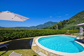 Ein Swimmingpool mit Steinrand, eine Liege und ein großer Sonnenschirm.