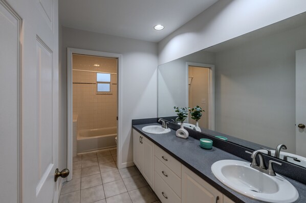 A modern bathroom with two sinks, a large mirror, and a bathtub.