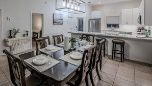 A modern kitchen with white cabinets, stainless steel appliances, and a dining area with a dark wooden table and matching chairs. - Spacious 2-Story Villa with Pool & Putting Green (Naples)