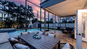 A poolside patio with outdoor furniture, a covered seating area, and a view of the pool and palm trees. - Spacious 2-Story Villa with Pool & Putting Green (Naples)