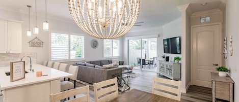 A spacious living area with a large chandelier, a dining table, and a sofa.