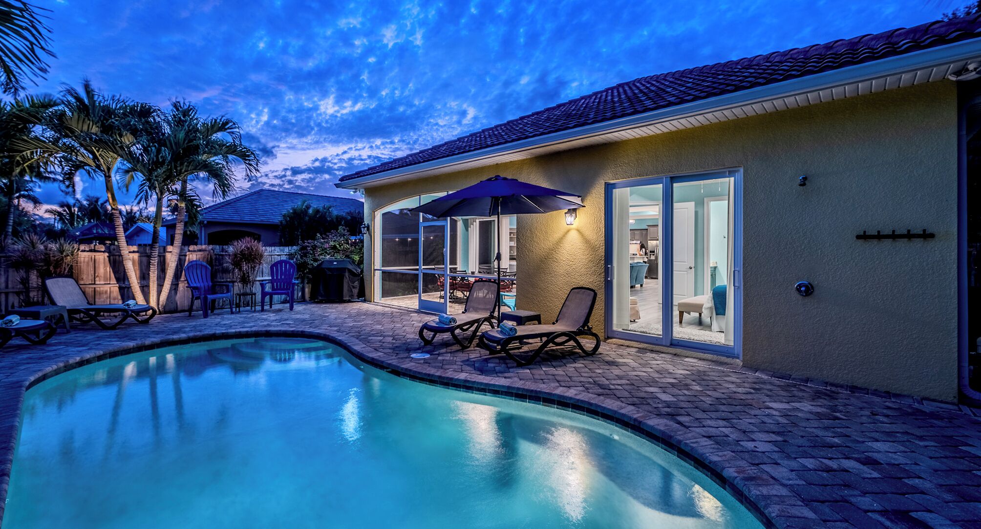 A swimming pool with lounge chairs, a patio area, and a house with a tiled roof and sliding glass doors.