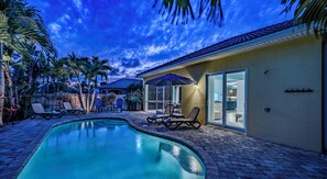A swimming pool with lounge chairs, a patio area, and a house with a sliding glass door. - Bright Naples Home w/ Heated Pool & Lanai (Naples)