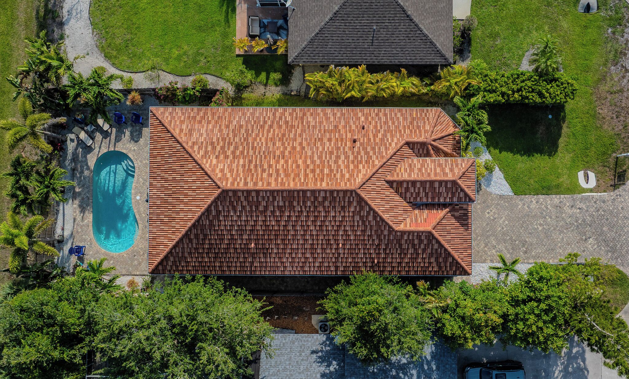 Ovenudblik over et hus med swimmingpool, omgivet af grønt og en belagt sti.
