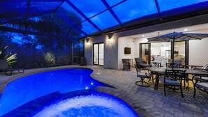 Ein Schwimmbad mit Whirlpool, Sitzgelegenheiten im Freien und einer überdachten Terrasse mit Glaswänden.