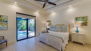 Ein Schlafzimmer mit Bett, Nachttischen, Deckenventilator und Blick auf einen Pool durch eine Glastür.