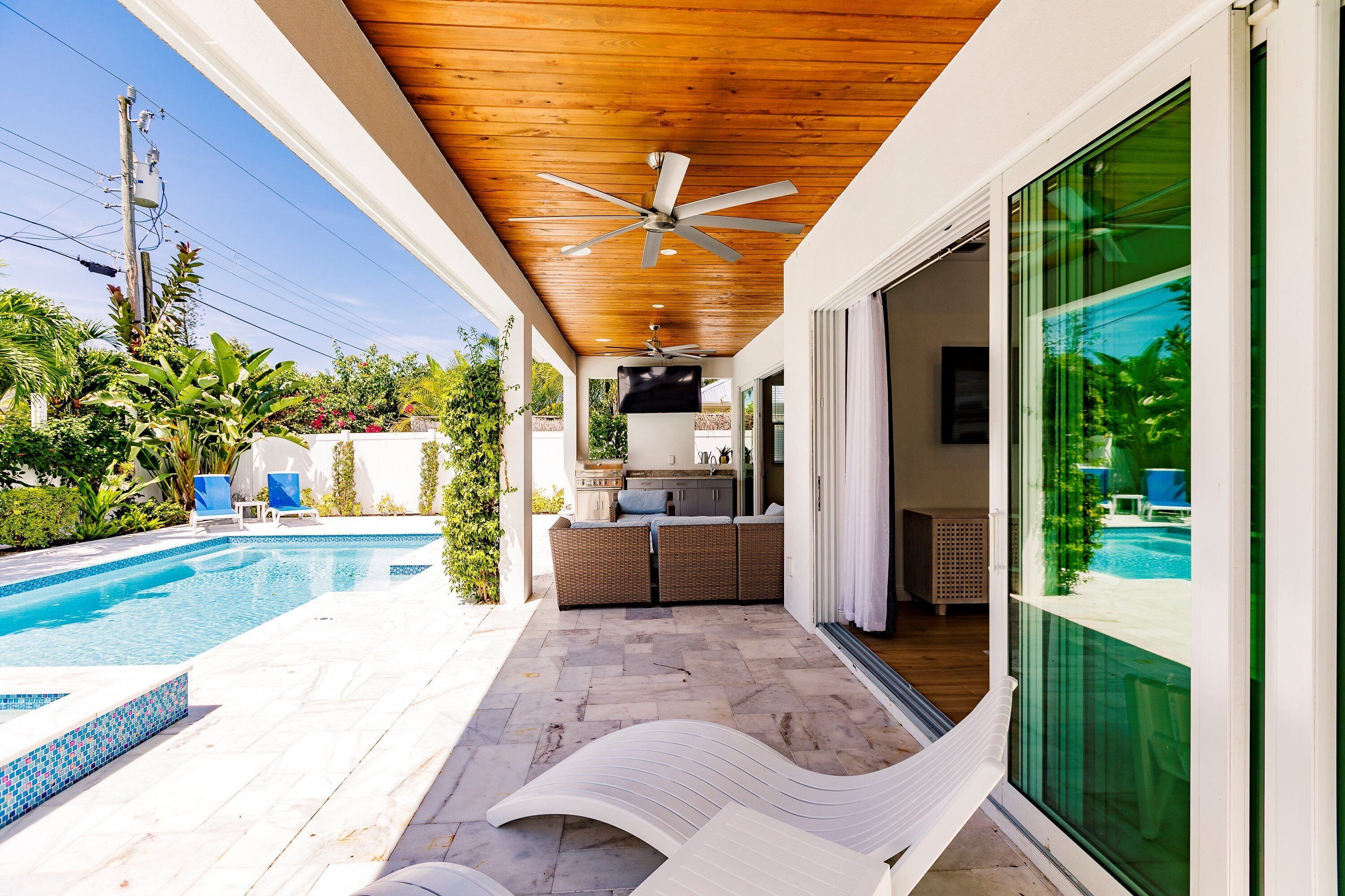 A covered outdoor area with a pool, lounge chairs, and a ceiling fan.