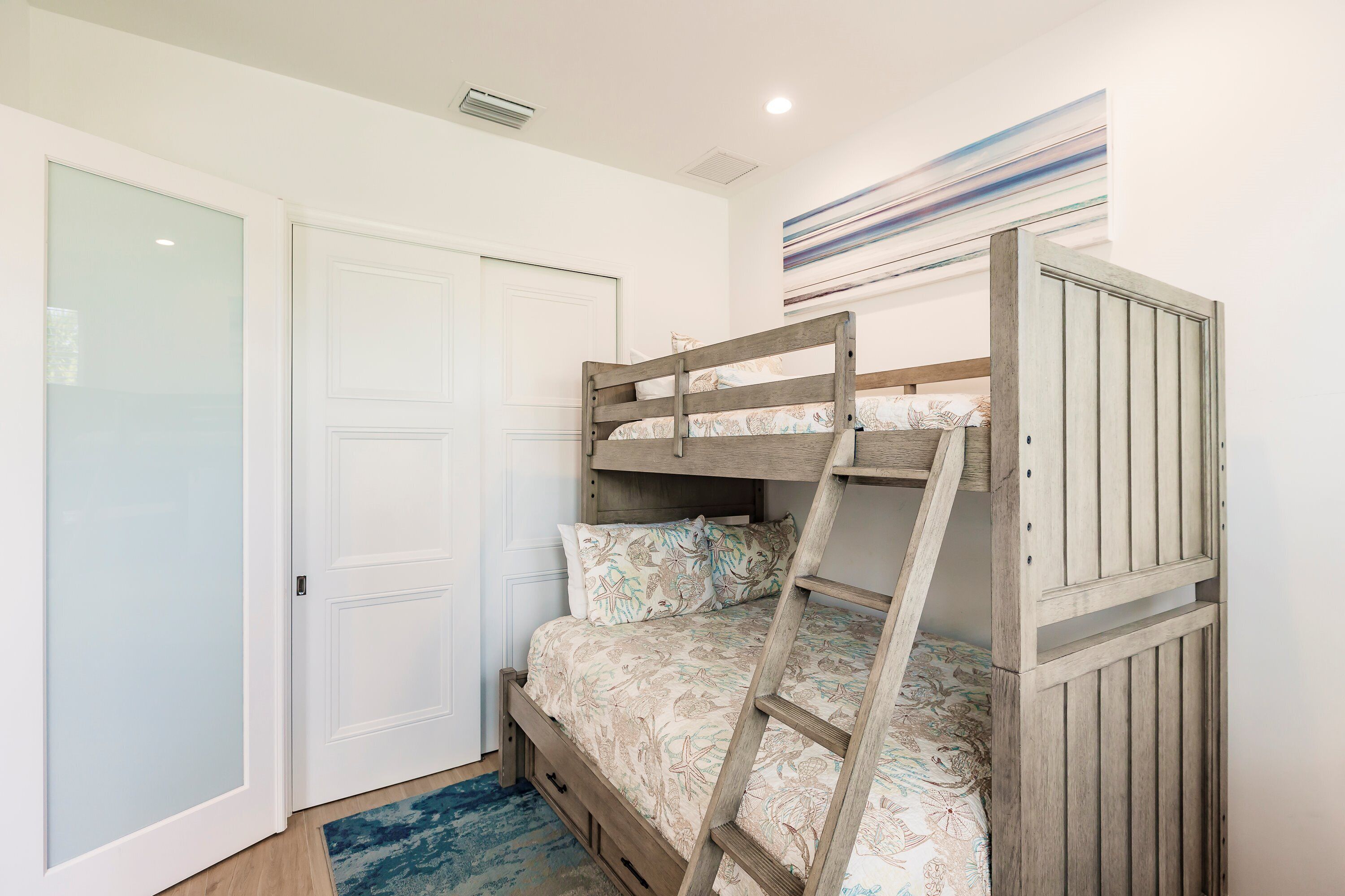 A bunk bed with a ladder, a white door, and a blue patterned rug.