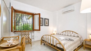 Een kamer met een bed, raam, stoel, tafel en een wandairconditioner.