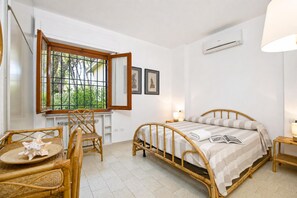 Une pièce comprenant un lit, une fenêtre, une chaise, une table et un climatiseur fixé au mur.