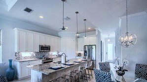 A modern kitchen with white cabinets, a large island with bar stools, and pendant lighting. - Casa Allegra | Bright, Modern 4 BR Pool Home in Naples Park (Naples)
